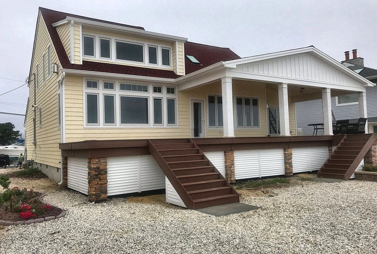Yellow siding and white trim going on, with stone piers under the deck